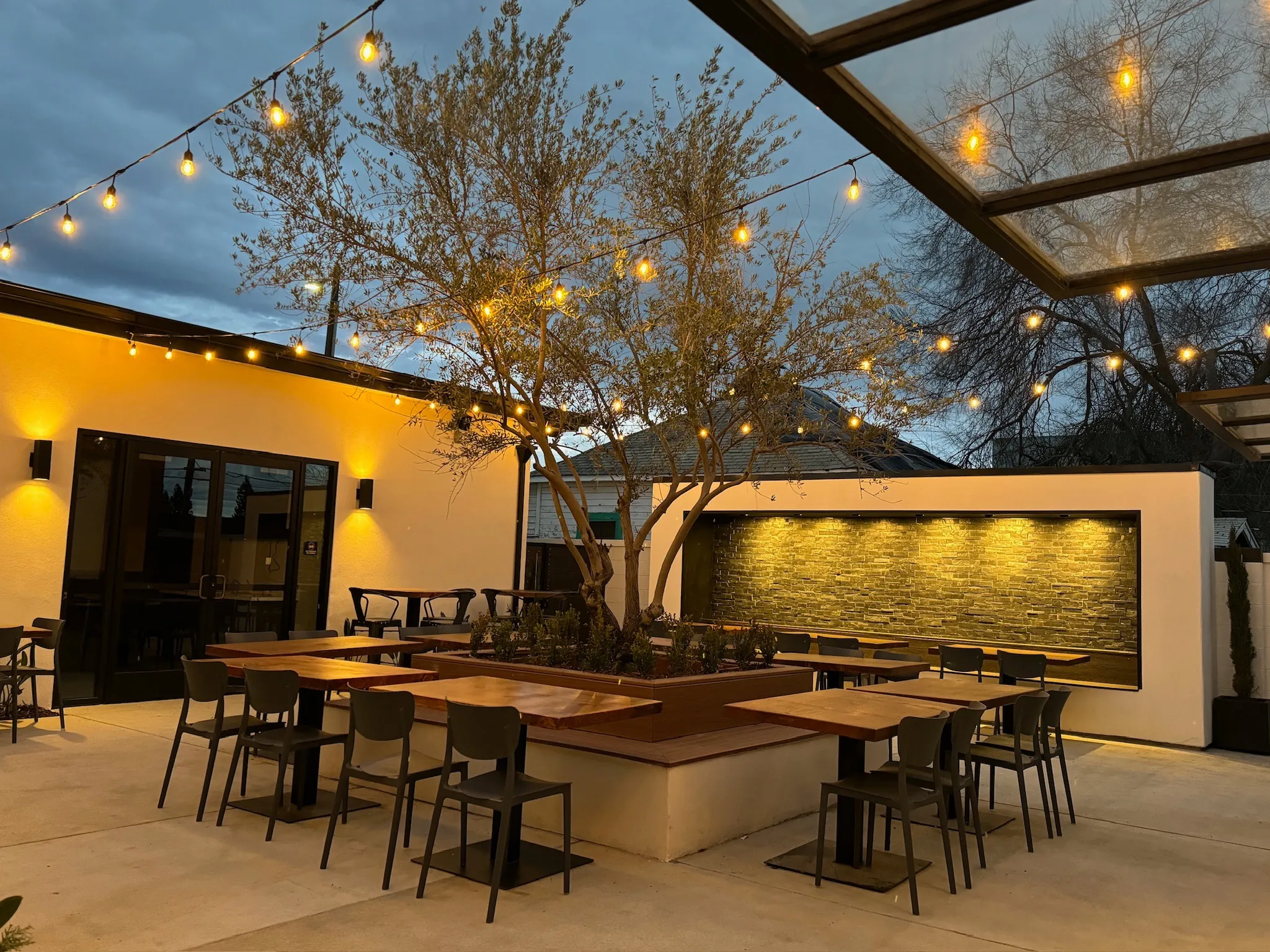 Courtyard at dusk with string lights, olive tree and stone waterfall wall